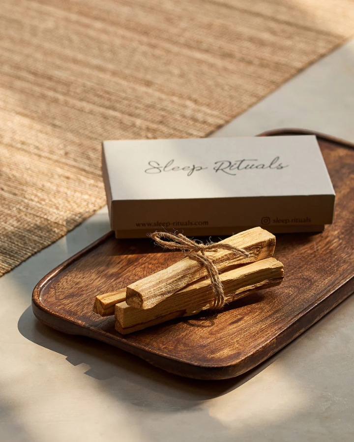 Palo Santo sticks tied with twine on a wooden tray with 'Sleep Rituals' box in the background.